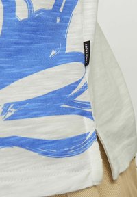 Vit T-shirt med blå abstrakt grafisk design, med en texturerad tygkonstruktion och en liten svart etikett med "JACK & JONES" på sidan.