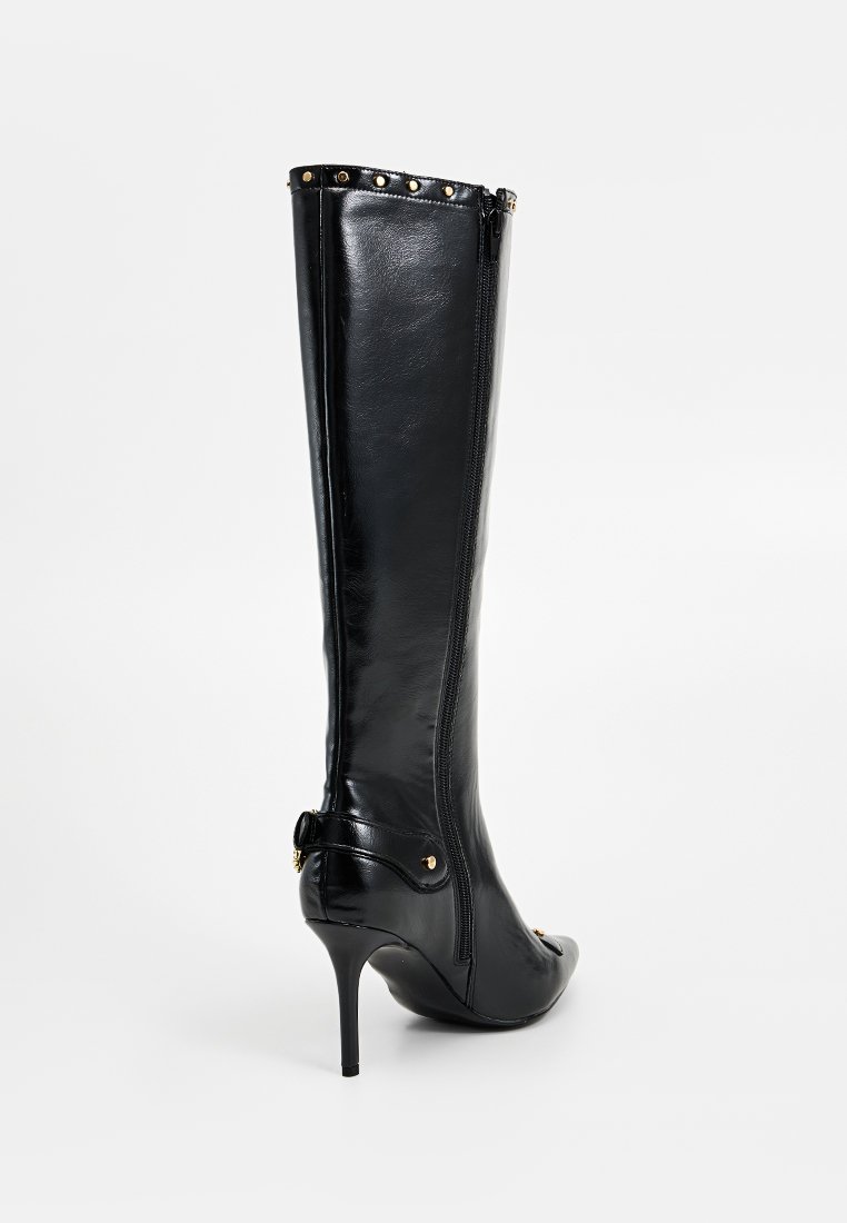 Czarny skórzany trzewik do kolan na wysokim obcasie typu stiletto, z bocznym zamkiem błyskawicznym, złotymi ćwiekami na górnej krawędzi i dekoracyjnym paskiem w okolicy obcasa.