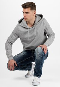 Felpa grigia in pile con un cappuccio ampio, abbinata a jeans blu sbiaditi con dettagli di cucitura. Sneaker bianche completano l'outfit.