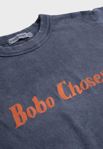 Maglietta in cotone blu marina con collo a girocostina e scritta arancione "Bobo Choses" stampata sul petto.