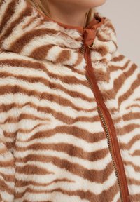 Mikina s kapucí z umělé kožešiny s hnědým a krémovým pruhovaným vzorem tygra. Disponuje zipovým zapínáním s kontrastním lemem a hebkým povrchem.