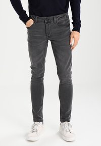 Slimmad grå jeans med sliten finish, fem fickor och knappgylf. Matchade med vita sneakers och en mörk tröja.