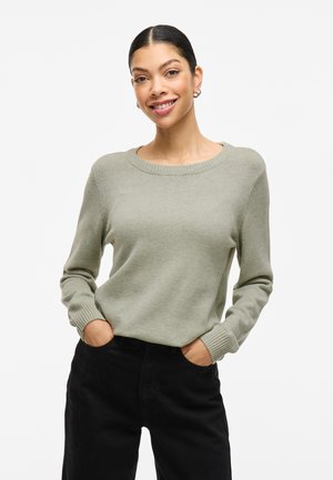 Pull en tricot vert clair avec un col rond et des poignets côtelés, associé à un pantalon noir, présenté sur un fond neutre.