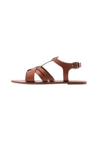 Sandali in pelle marrone con cinturini incrociati, fibbia alla caviglia regolabile e suola piatta. Design elegante con punta aperta.