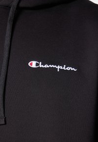 Sweat-shirt noir à capuche en tissu doux. Comprend un logo "Champion" brodé en blanc avec un accent rouge. Cordonc à la capuche.
