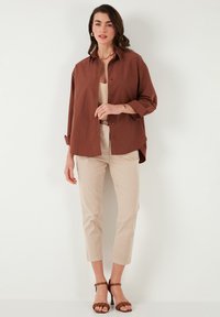 Brown button-up shirt, cream top, beige trousers, and brown strappy heels. The fabric appears lightweight with a relaxed fit.