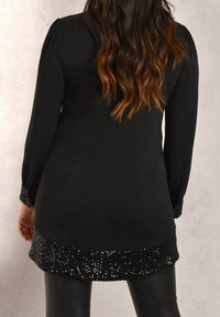 Black tunic with long sleeves, featuring a sequin-accented hem and textured finish. Silhouette hugs the body, complementing fitted leggings.