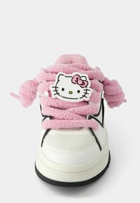 Bílé tenisky s texturovaným svrškem, černými akcenty a růžovými huňatými tkaničkami. Na jazyku je výrazná hlava Hello Kitty.