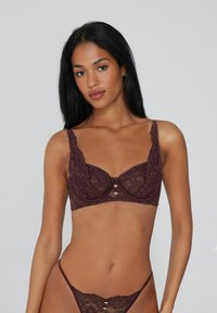 Bordový krajkový podprsenka s květinovým vzorem, s podprsenkovou výztuhou, širokými ramínky a zlatými srdíčkovými akcenty uprostřed. Součástí je tanga.