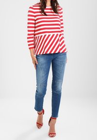 Rot-weißer gestreifter Langarmshirt mit Peplum-Design, kombiniert mit hellblauen Jeans und roten Absatzsandalen.