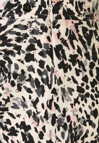 Detailní záběr na látku s leopardím potiskem v černé, šedé a růžové barvě, se bílým zipem a kulatým černým knoflíkem "ck".