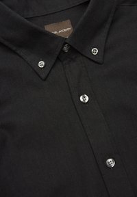 Czarna koszula zapinana na guziki z ostrym kołnierzykiem, posiada srebrne guziki i teksturowaną tkaninę. Etykieta marki jest widoczna w pobliżu kołnierzyka.