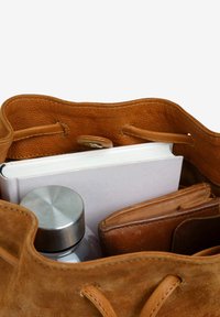 Brown suede bag interior featuring a gray metal water bottle, a white book, and a brown leather wallet, with drawstring closure.
