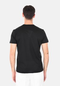T-shirt nera a maniche corte in cotone, con collo tondo e texture liscia. Sul retro presenta un dettaglio del logo discreto.