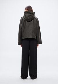 Oliiviroheline lühike jakk kapuutsiga, lahtise lõikega ja laiade varrukatega. Kõrge kaelus ja sile pind. Kandmiseks mustade laiade pükste peal.