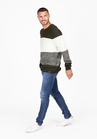 Maglione lavorato a maglia con tre strisce orizzontali in verde scuro, bianco e grigio, abbinato a jeans blu e sneaker bianche.