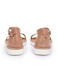 Brązowe skórzane sandały z paskiem na kostce i zapięciem z tyłu, białą platformą i czerwonym akcentem w postaci ściegów na pięcie.