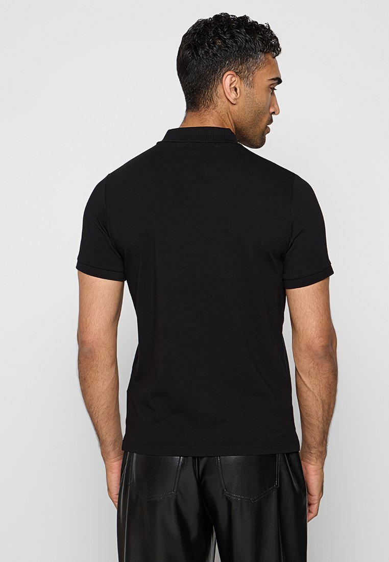Polo shirt noir à manches courtes, en coton, design classique, col côtelé, texture subtile, forme ajustée, sans motifs ni accents visibles.