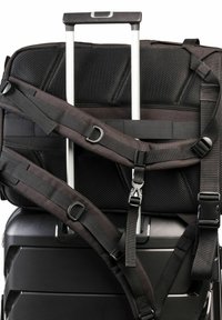Maleta de viaje negra con correas ajustables, que presenta una superficie texturizada y un mango de aluminio sobre una maleta rígida con ranuras.
