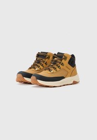 Scarpe da trekking marroni e nere con design a taglio medio, materiale testurizzato, accessori metallici color oro e suola in gomma con motivo a zigzag.