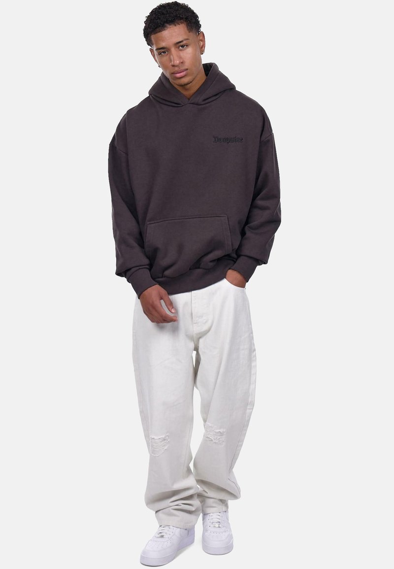 Brązowy hoodie z kangurzą kieszenią i wytłoczonym logo, w połączeniu z białymi, postarzanymi spodniami szerokimi i białymi sneakerami.