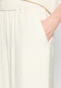 Lichtromige wijde broek van stof met een gestructureerde textuur, elastische tailleband en zijzakken. De stof heeft een kreukelige uitstraling.