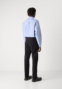Striped blue shirt with long sleeves, paired with black pants and black shoes. The shirt has a relaxed fit and button detail at the cuffs.