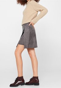 Grijze Suède rok met geplooid ontwerp, beige gebreide trui en glanzende bordeauxrode veterschoenen met een chunky zool.