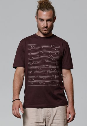 T-shirt en coton bordeaux avec un graphique de lignes blanches représentant des formes de chats stylisées. Manches courtes et encolure ronde. Dos uni.