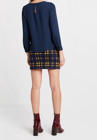 Námořnická blůza s detailem ve tvaru klíčové dírky na zádech, zkombinovaná s přiléhavými kostkovanými sukněmi v námořnické, žluté a bílé barvě, doplněná burgundskými kotníkovými botami.