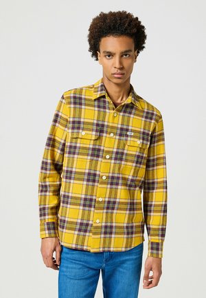 Camicia di flanella a quadri gialla con accenti viola e verdi, due tasche sul petto e chiusura a bottoni. Tessuto morbido e design a vestibilità regolare.