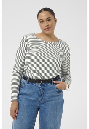 Femeie cu păr negru prins într-un coc jos, purtând cercuri de urechi aurii, o bluză cu mâneci lungi în dungi alb-negru, blugi albaștri și o curea neagră.