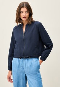 Mörkblå kort jacka med dragkedja fram, elastiska ärmslut och dragsko i nederkant; har sidofickor och en slät tygtextur.