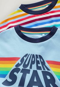 Due T-shirt impilati, una azzurro chiaro con una stampa di un arcobaleno e la scritta "SUPER STAR", e l'altra a righe multicolori con colletto blu navy.