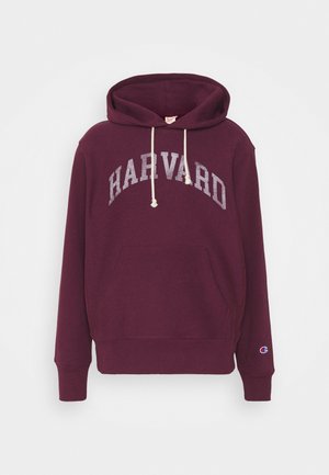 Bordeauxroter Hoodie mit weißen Kordeln, "HARVARD"-Schriftzug auf der Brust, Kängurutasche vorne und kleinem Champion-Logo am linken Ärmelbündchen.