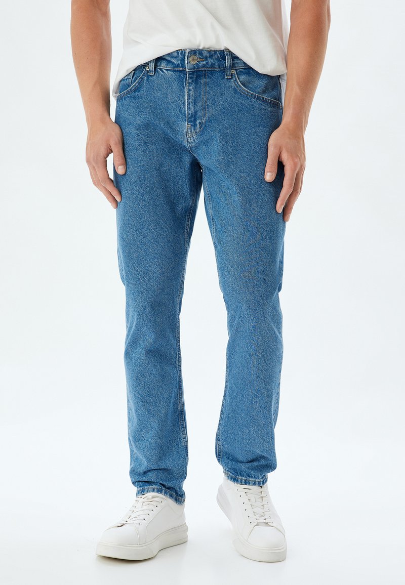Jeans in denim blu chiaro con taglio dritto, design a cinque tasche e chiusura con bottone. Abbinati a sneaker bianche a bassa cima.