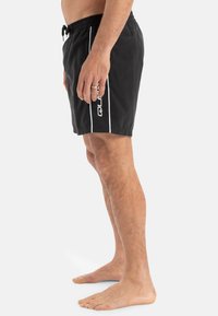 Bañador negro con cintura ajustable, rayas blancas laterales y detalle de logo. Textura suave, corte a la altura de la rodilla y material ligero.