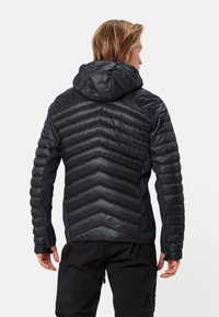 Giacca nera isolata con design a motivo chevron, cappuccio e polsini elasticizzati. Il materiale sembra elegante, leggero e resistente all'acqua.