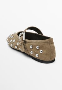 Scarpa piatta in suede color taupe con dettagli in metallo argento, cinturino posteriore, punta arrotondata e suola nera bassa. Superficie testurizzata con finitureMetalliche.