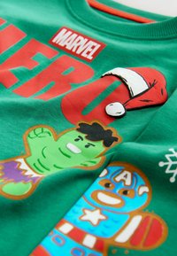 Zielona bluza z czerwonym napisem "MARVEL HERO", detalem w postaci puszystej czapki Świętego Mikołaja oraz postaciami z kreskówek: Hulka i piernikowego Captain America.