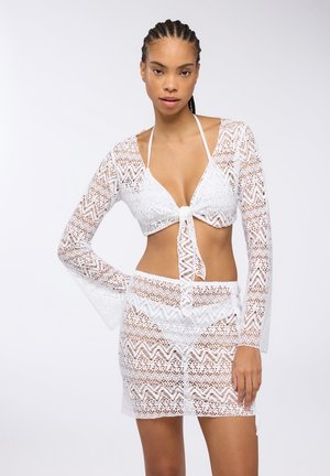 Set di bikini bianco all'uncinetto con top davanti annodato e maniche lunghe, abbinato a una gonna. Motivo a zigzag, texture leggera e design aderente.