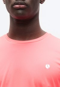 Φωτεινό ροζ, υφασμάτινο αθλητικό πουκάμισο με στρογγυλή λαιμόκοψη. Διαθέτει μικρό λευκό λογότυπο στην αριστερή περιοχή του στήθους. Ελαφρύ ύφασμα.