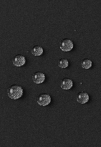 Krople wody na czarnej teksturowanej tkaninie, pokazujące wodoodporność z kroplami zbierającymi się na powierzchni.