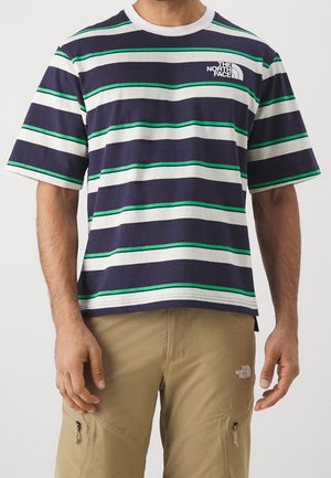 Mann trägt ein navyblaues, weißes und grünes gestreiftes T-Shirt und khakifarbene Cargohosen, beide mit dem The North Face Logo.