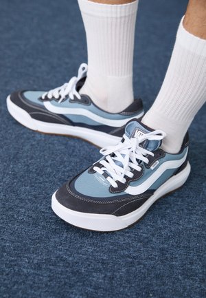 Blue and gray athletic shoes with suede and fabric materials, featuring white laces, rubber soles, and a curved design, paired with white socks.