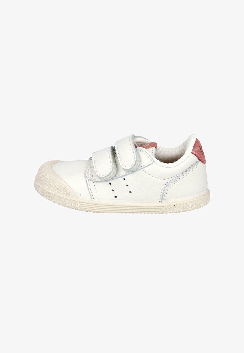 Zapatillas blancas para niños con suela beige, dos correas de Velcro, pequeños orificios de ventilación laterales y un acento rosa en la lengüeta del talón.