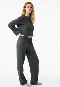 Szary, prążkowany zestaw do domu składający się z krótkiego topu z długim rękawem oraz luźnych spodni z elastycznym paskiem i sznurkiem.