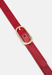 Ceinture en cuir rouge avec une boucle en métal doré en forme ovale. La ceinture présente des trous pour ajustement et une finition lisse et texturée.