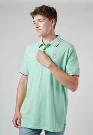 Polo shirt vert clair avec un col côtelé présentant des rayures rouges et blanches, logo brodé et manches courtes. Tissu en coton doux.