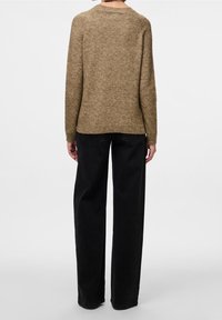 Pull marron texturé avec un col rond, des manches longues et une coupe décontractée, associé à un pantalon noir taille haute avec des jambes droites.